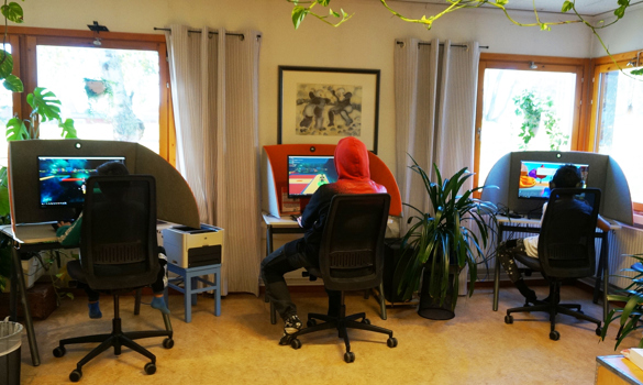 Tre unga pojkar sitter med ryggen till och spelar dataspel på bibliotekets datorer.